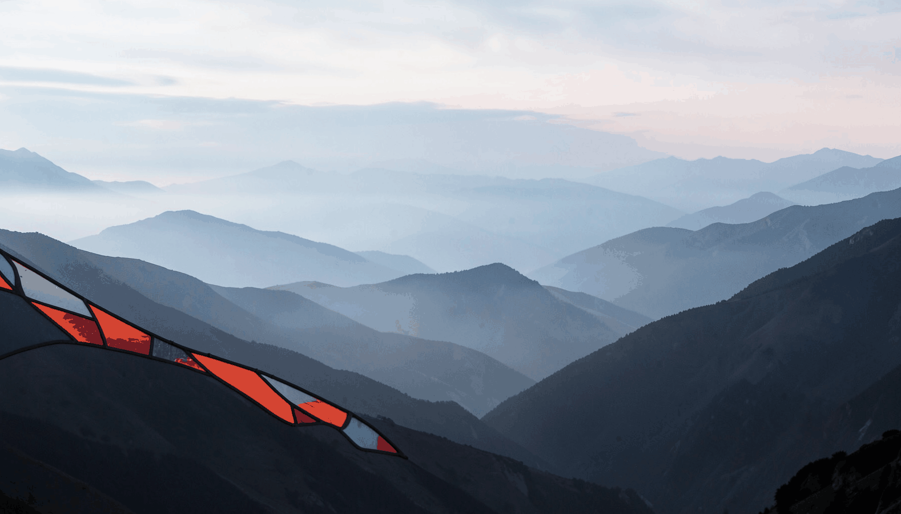 A wide-angle mountain panorama with layered ridges fading into misty blues and soft greys