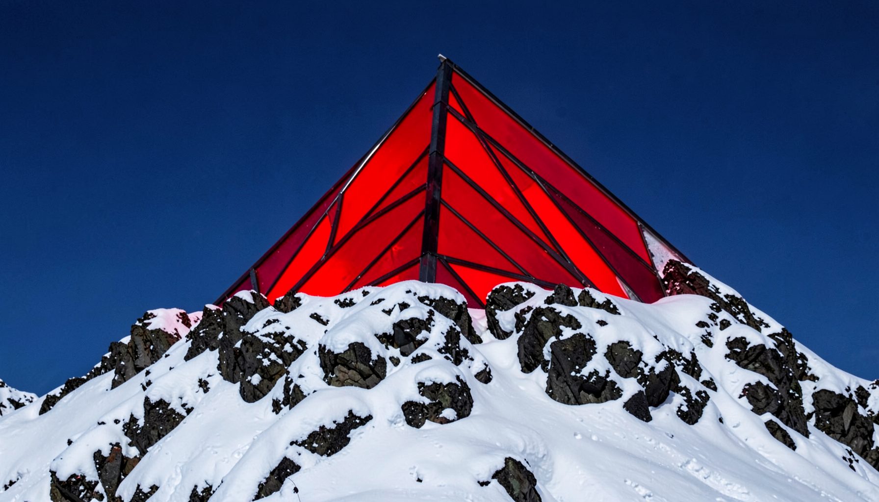 A snow-dusted summit pyramid against a deep blue sky, crisp white and charcoal rock tones